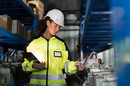 Woman worker using digital tablet working  and inspecting at shelves of electronic equipment parts in warehouse