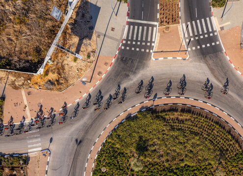 Aerial view of a group of cyclists riding along a road with long shadows cast on the asphalt near a roundabout in Rosh Haayin, Center District, Israel.
