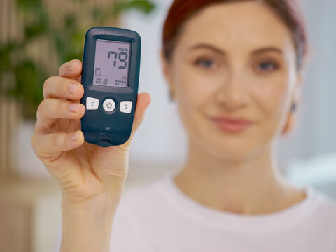 A woman shows a glucometer reading of 79 mg dL, which indicates good blood sugar levels. She demonstrates the importance of monitoring glucose for diabetes care.