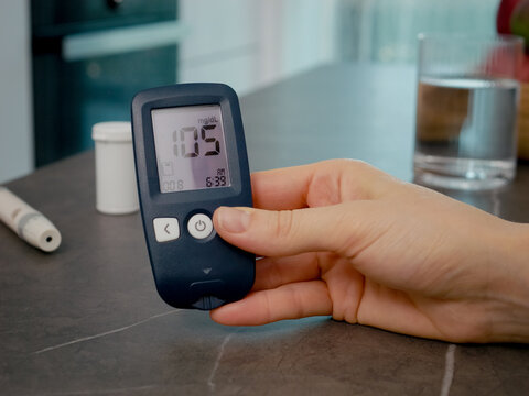 Female swipes through her glucometer diary in the kitchen. She reviews her past blood sugar results to monitor her diabetes management.