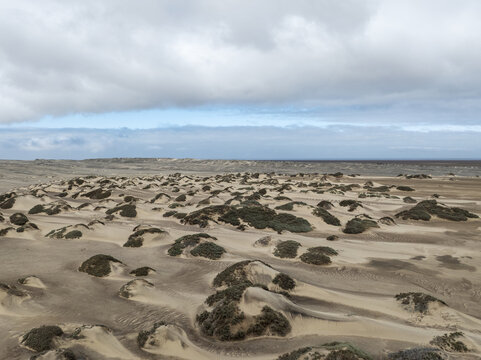 Aerial view of Skeleton Coast featuring sand dunes with sparse vegetation under a cloudy sky in Kunene Region, Namibia.