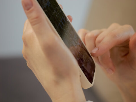A woman is using her smartphone at home. She holds the phone in one hand and swipes with her fingers, staying connected and engaged.