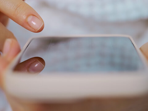 A person is using a smartphone with both hands while interacting with others in a home setting. Focus is on the hands and device during the activity.
