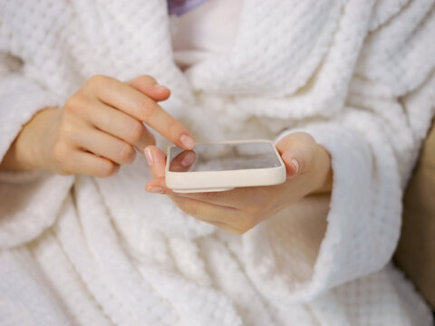 A woman is holding a smartphone while swiping through the screen. She is socializing at home. Her hands are relaxed and engaged with the device.