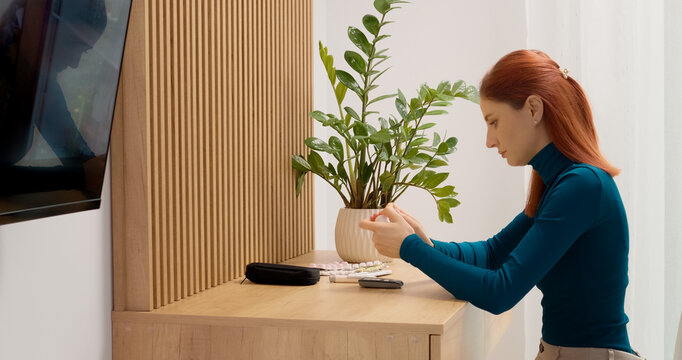 A woman sits at a table and takes a blood sugar test using a glucometer. She puts the test strip into the device to check her glucose level.