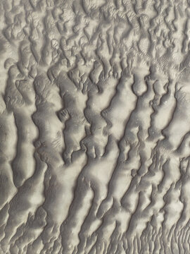 Aerial view of the textured sand dunes of the Skeleton Coast, showcasing intricate wind-blown patterns and soft shadows across the desert landscape in Kunene Region, Namibia.