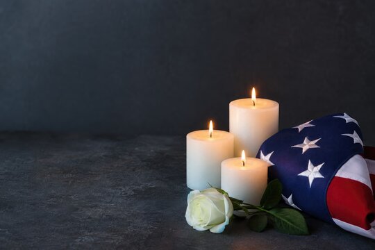 Candles illuminate remembrance alongside folded flag and white rose, symbolizing honor