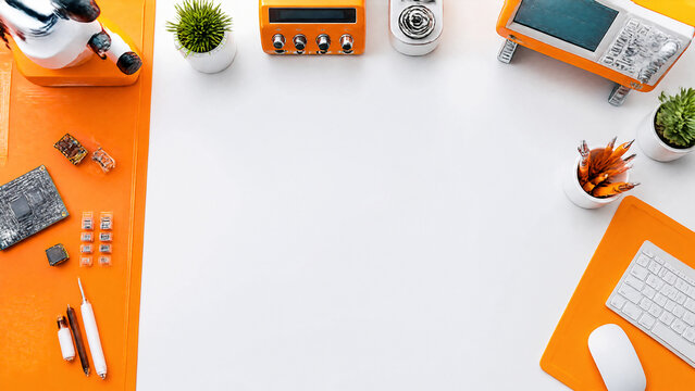 Top view of a professional engineering workstation with electronic tools, circuit boards, and orange accents on a clean white background, perfect for technology, innovation, and STEM education
