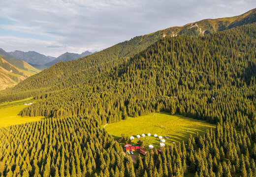 Aerial view of Kok Jaiyk valley featuring a traditional yurt camp nestled among dense coniferous forests and rolling mountain slopes in Dzhetyoguz, Issyk-Kul Region, Kyrgyzstan.