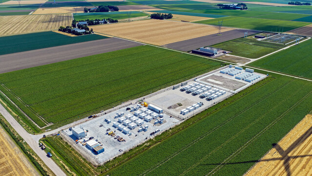 Aerial view of a battery energy storage system facility situated in a rural agricultural landscape with surrounding crop fields and a nearby power substation in Dronten, Flevoland, Netherlands.