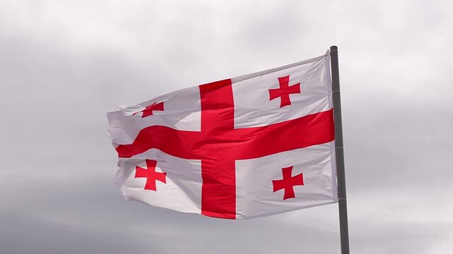 Georgian national flag, known as the five cross flag, waving proudly on a flagpole against a dramatic gray and cloudy sky, symbolizing the country's patriotism and national identity slow motion