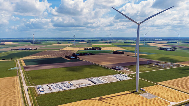 Aerial view of a wind farm with a large turbine and a battery storage facility set amidst agricultural fields in Dronten, Flevoland, Netherlands.
