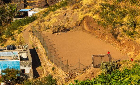 Aerial view of a dirt soccer field nestled in the rugged mountains of Santo Antao, with stone retaining walls and sparse vegetation in Alto Mira, Porto Novo, Cabo Verde.