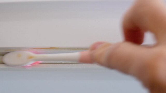 Closeup of dirty refrigerator seal showing homeowner using toothbrush to gently remove brown grime and mold from rubber gasket inside white kitchen, steady slow strokes, natural