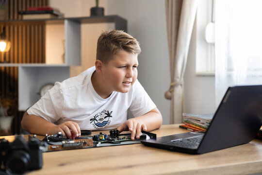 Curious boy focusing on disassembling electronic device circuit while watching a tutorial on a laptop at home