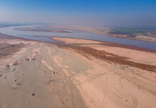 Aerial view of the Banbawali - Ravi - Bedian Canal Ravi river Siphon Lahore with vast sandy banks, tire tracks, and calm water under a clear blue sky in Ferozewala, Punjab, Pakistan.