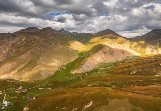 Aerial view of the rugged mountain landscape near Tash Rabat Caravan Palace with a winding river in the green valley in At-Bashi District, Naryn Region, Kyrgyzstan.
