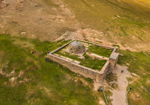 Aerial view of Tash Rabat Caravan Palace, a historic stone structure with a central dome and courtyard, situated in a vast green mountain valley in At-Bashi District, Naryn Region, Kyrgyzstan.