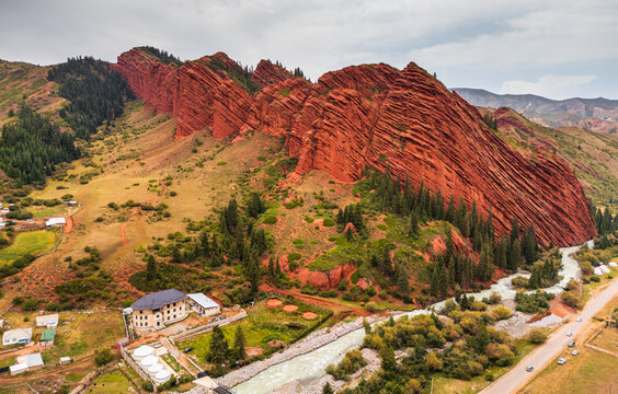 Aerial view of the iconic Seven Bulls Rock sandstone formations rising above a winding river, green slopes, and a small settlement in Dzhetyoguz, Issyk-Kul Region, Kyrgyzstan.