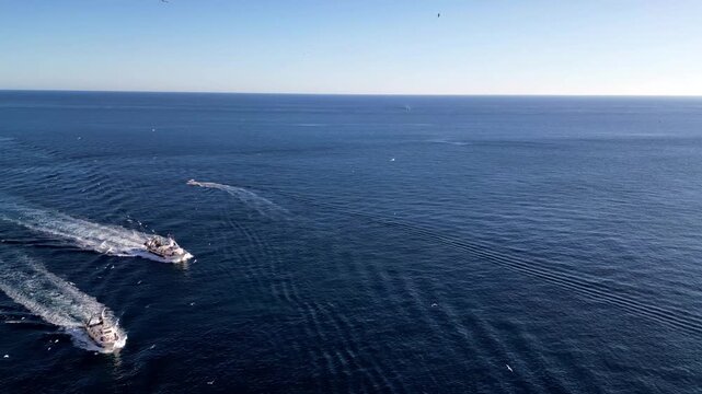 Aerial view of three boats moving in formation through the deep blue Mediterranean Sea, leaving white wakes behind them in Calp, Valencian Community, Spain.