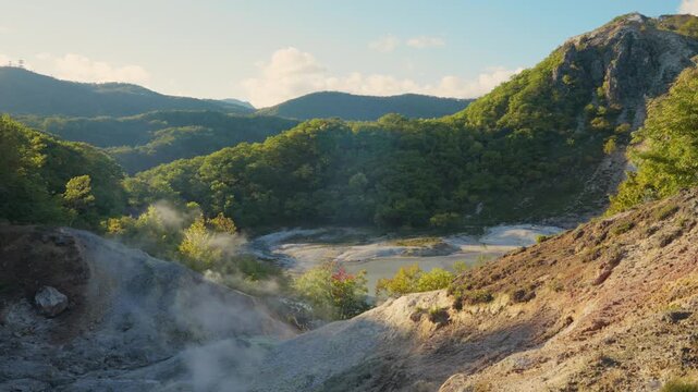 Picturesque landscape view of a volcanic valley with steam rising from geothermal hot springs at Jigokudani Hell Valley, a famous onsen resort area located in Noboribetsu, Hokkaido