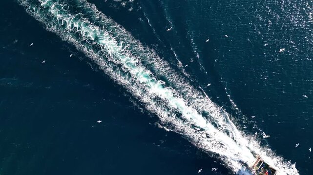 Aerial view of a fishing boat navigating through the deep blue sea, leaving a white wake behind it in Calp, Valencian Community, Spain.