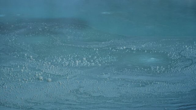 Turquoise thermal water boiling and bubbling with sulfurous steam rising from the volcanic lake in Noboribetsu Onsen, a famous geothermal active area and tourist attraction in Hokkaido, Japan