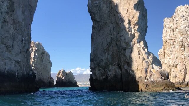 Sea cliffs rise above blue ocean along rocky coastline. Rugged rock formations frame coastal water with distant shoreline beneath clear blue sky.