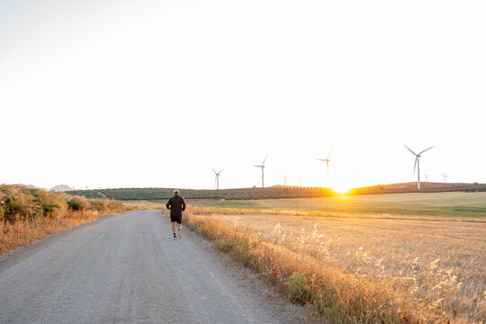 Runner exercising along countryside road with wind turbines at sunset
