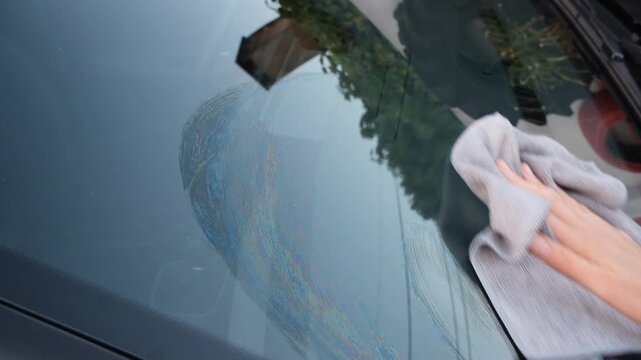 Close-up of a hand cleaning a car windshield with a microfiber cloth, removing dirt and streaks during vehicle maintenance, emphasizing cleanliness, care, and detailing