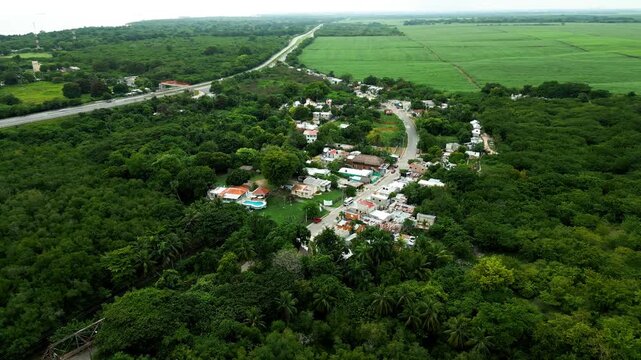 Aerial view of Rio Soco winding through lush green vegetation, agricultural fields, and a small residential area in San Pedro de Macoris, San Pedro de Macoris, Dominican Republic.