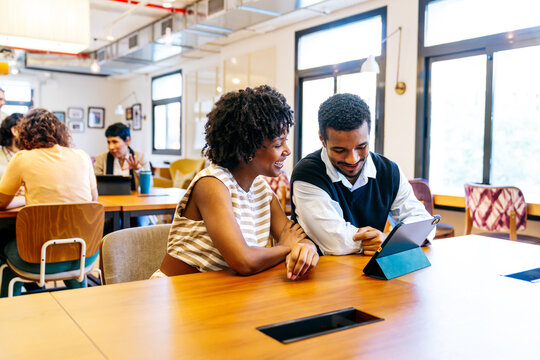 Young black woman and man smiling while working together on a digital tablet at a modern coworking office