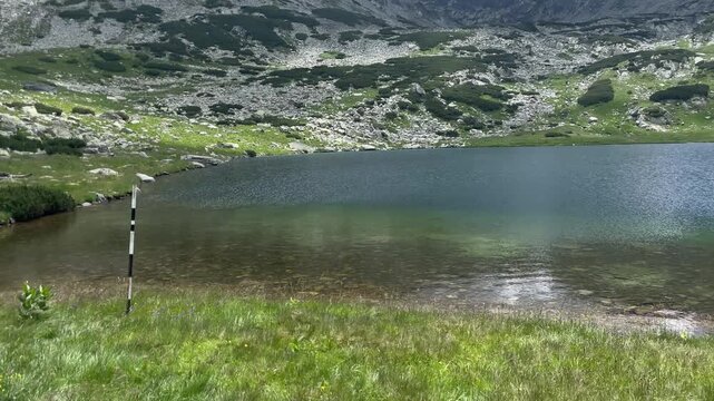 Panning shot of the crystal clear glacial lake Gales surrounded by rocky alpine landscape and green shores in Retezat Mountains, Romania, nature and travel video, 4k, 60fps.