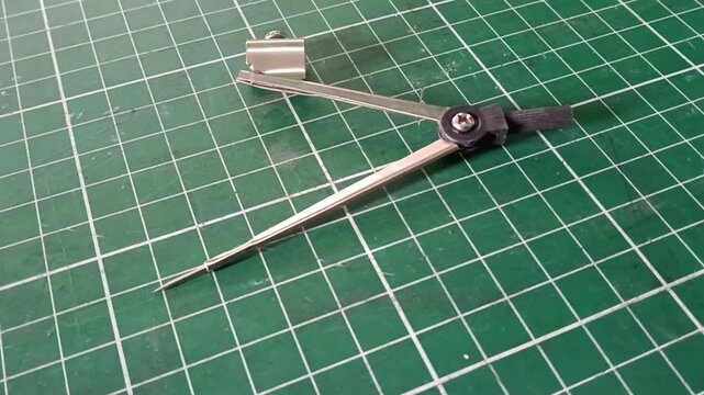 Metal drawing compass with a sharp needle point and pencil holder, used for drawing circles and arcs in technical drawing, drafting, geometry, and school work, isolated on a green cutting mat