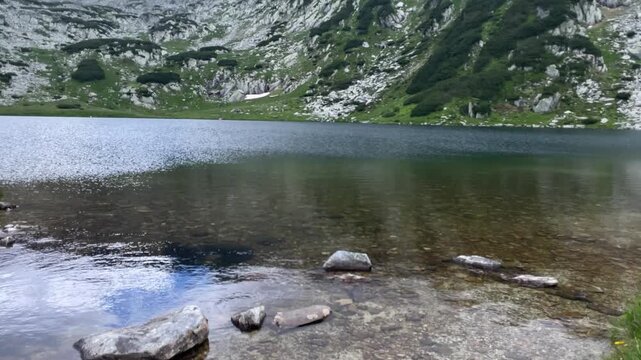 Panning shot of the crystal clear glacial lake Gales surrounded by rocky alpine landscape and green shores in Retezat Mountains, Romania, nature and travel video, 4k, 60fps.