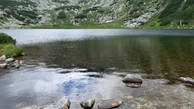 Panning shot of the crystal clear glacial lake Gales surrounded by rocky alpine landscape and green shores in Retezat Mountains, Romania, nature and travel video, 4k, 60fps.