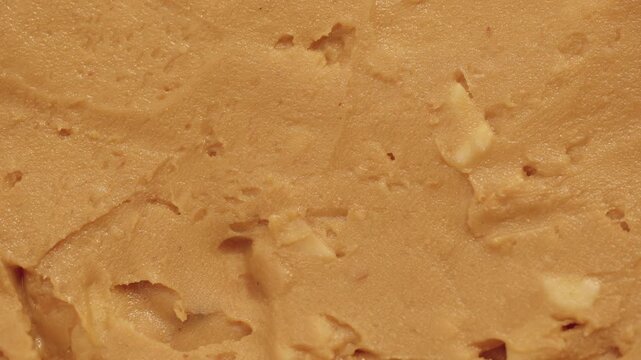 Peanut butter texture circle rotation close up top view. Crunchy peanut butter with peanut pieces. Classic peanut butter.