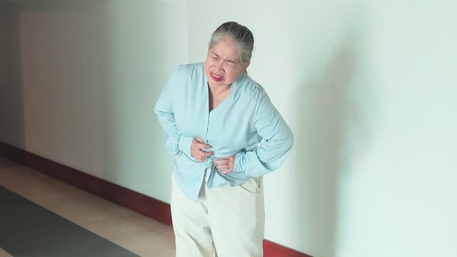 Southeast Asian senior woman suffering from stomach ache, concept video for elderly menopause, abdominal pain, food poisoning, gastritis, acid reflux or colon cancer