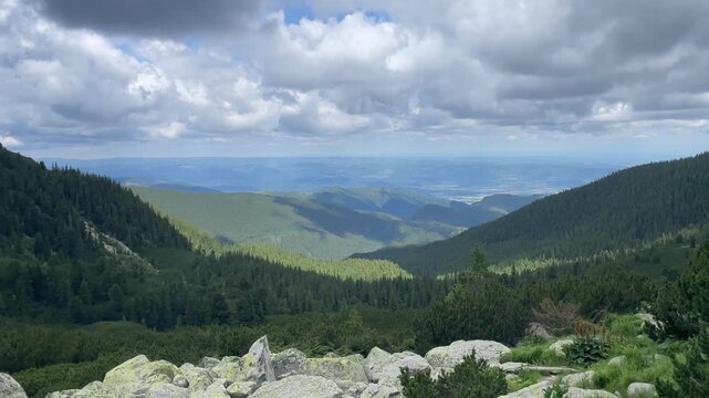 Panning shot of a scenic alpine landscape with green mountain slopes, coniferous forests, and dramatic cloudy sky in Retezat Mountains, Romania, nature and travel video, 4k, 60fps.
