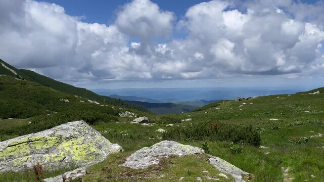 Panning shot of a scenic alpine landscape with green mountain slopes, coniferous forests, and dramatic cloudy sky in Retezat Mountains, Romania, nature and travel video, 4k, 60fps.