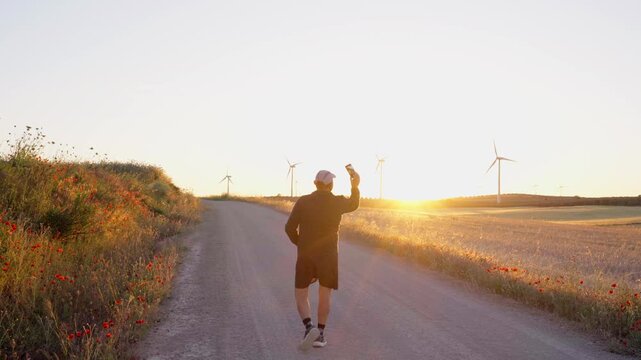 Man walking on rural road taking selfie at sunset
