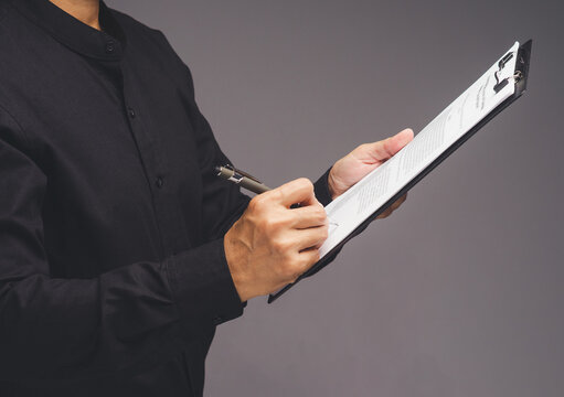 Person signing document on clipboard with pen