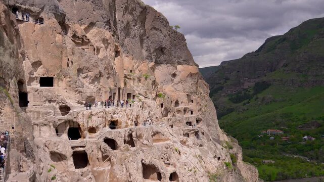 Vardzia, an ancient cave monastery complex in southern georgia, showing tourists walking along the rock-hewn passages carved into the cliffs of the erusheti mountain above the mtkvari river