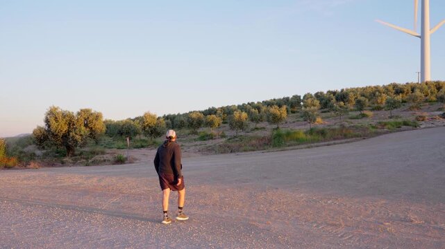 Man walking on a dirt road towards wind turbines at sunset