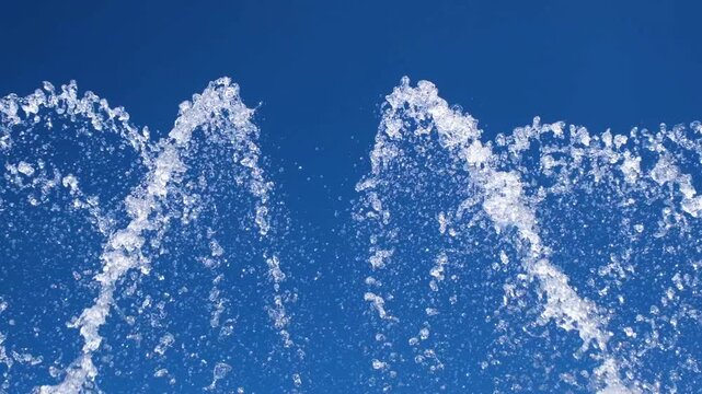 Close up of sparkling fountain water splashes against a blue sky. Refreshing droplets create a dynamic abstract background that represents freshness, summer, energy, and motion