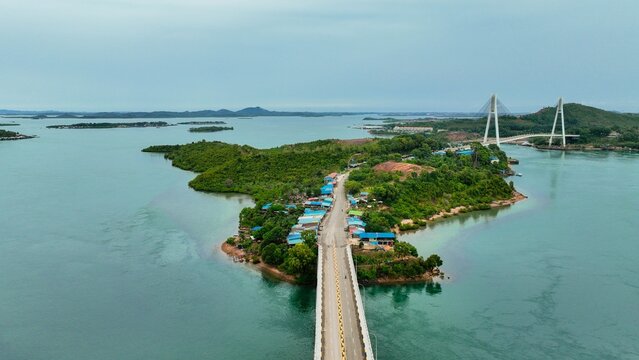 Aerial view of Barelang Bridge 1 connecting lush islands surrounded by turquoise waters under a cloudy sky in Kecamatan Bulang, Kepulauan Riau, Indonesia.