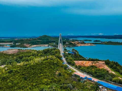 Aerial view of Barelang Bridge 1 spanning the blue waters surrounded by lush green hills and coastal landscape in Kecamatan Bulang, Kepulauan Riau, Indonesia.