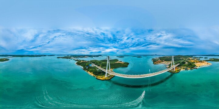 Aerial view of Barelang Bridge 1 connecting islands over turquoise waters with a small boat leaving a wake in Kecamatan Bulang, Kepulauan Riau, Indonesia.