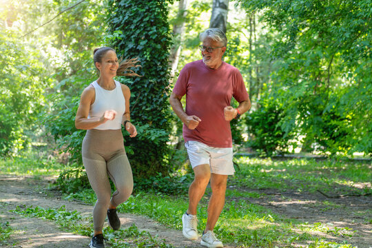 Senior man enjoying a guided cardio jogging workout with a fitness coach in a park to improve endurance, heart health, mobility, and functional fitness.