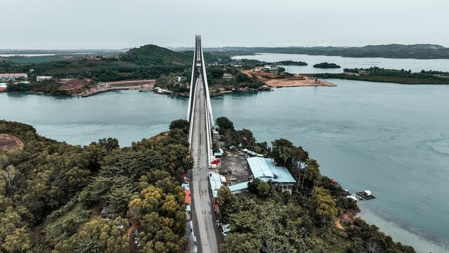 Aerial view of Barelang Bridge 1 spanning the calm waters of the strait, surrounded by lush tropical vegetation and coastal landscapes in Kecamatan Bulang, Kepulauan Riau, Indonesia.